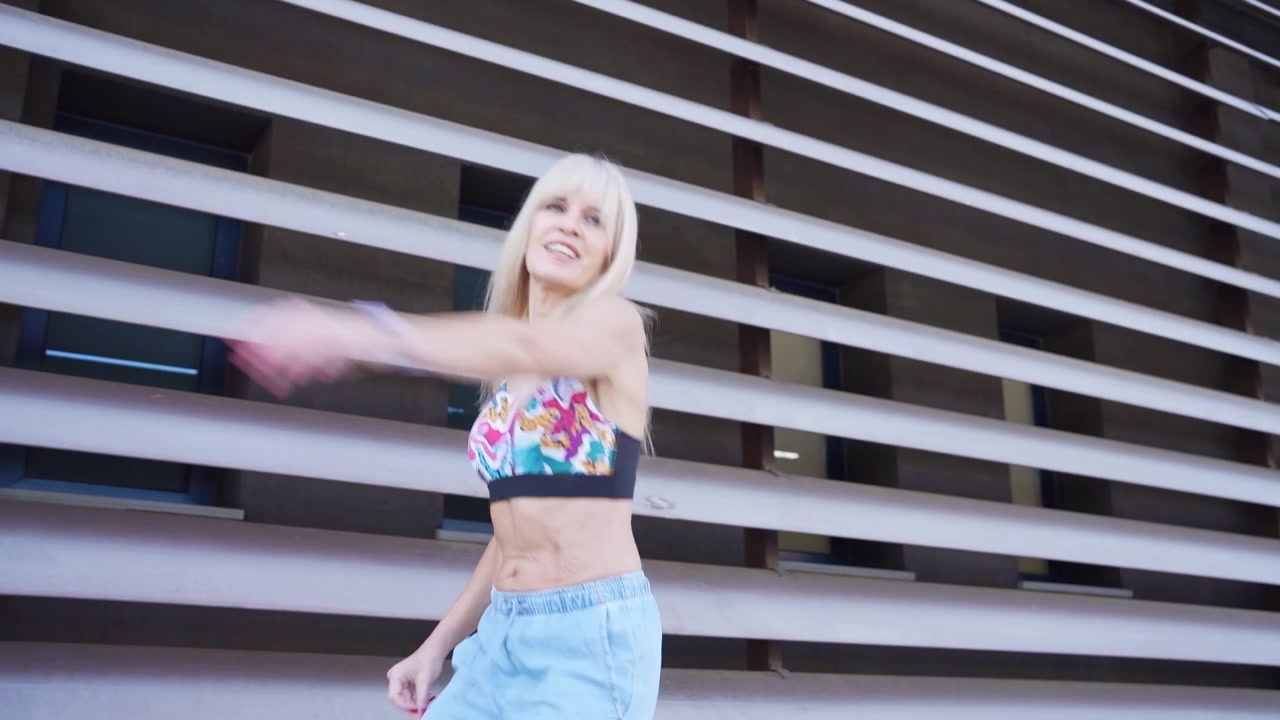 Ung kvinde danser ved siden af en moderne arkitektonisk baggrund i afslappet sommertøj.