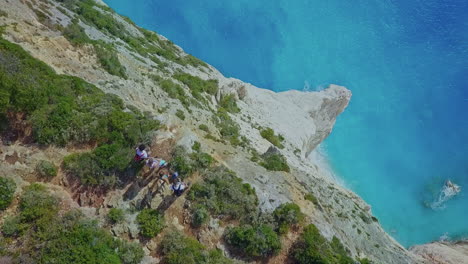 Aerial-looking-down-massive-ocean-cliff-with-people-on-edge-pans-up-to-horizon