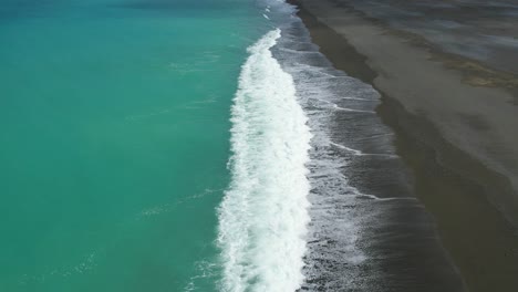 Zeitlupe-Aus-Der-Luft-über-Dem-Wunderschönen-Türkisfarbenen-Südpazifik,-Während-Wildwasser-Im-Kontrast-Zu-Dunkler-Steinküste-Steht---Birdlings-Flacher-Strand