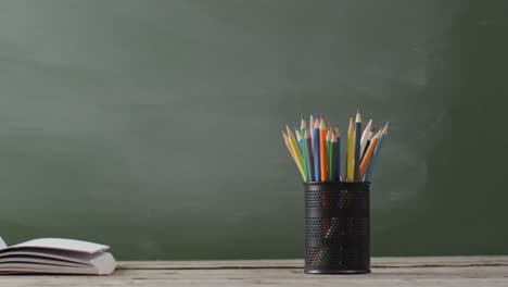 video of school supplies and books on wooden table over blackboard