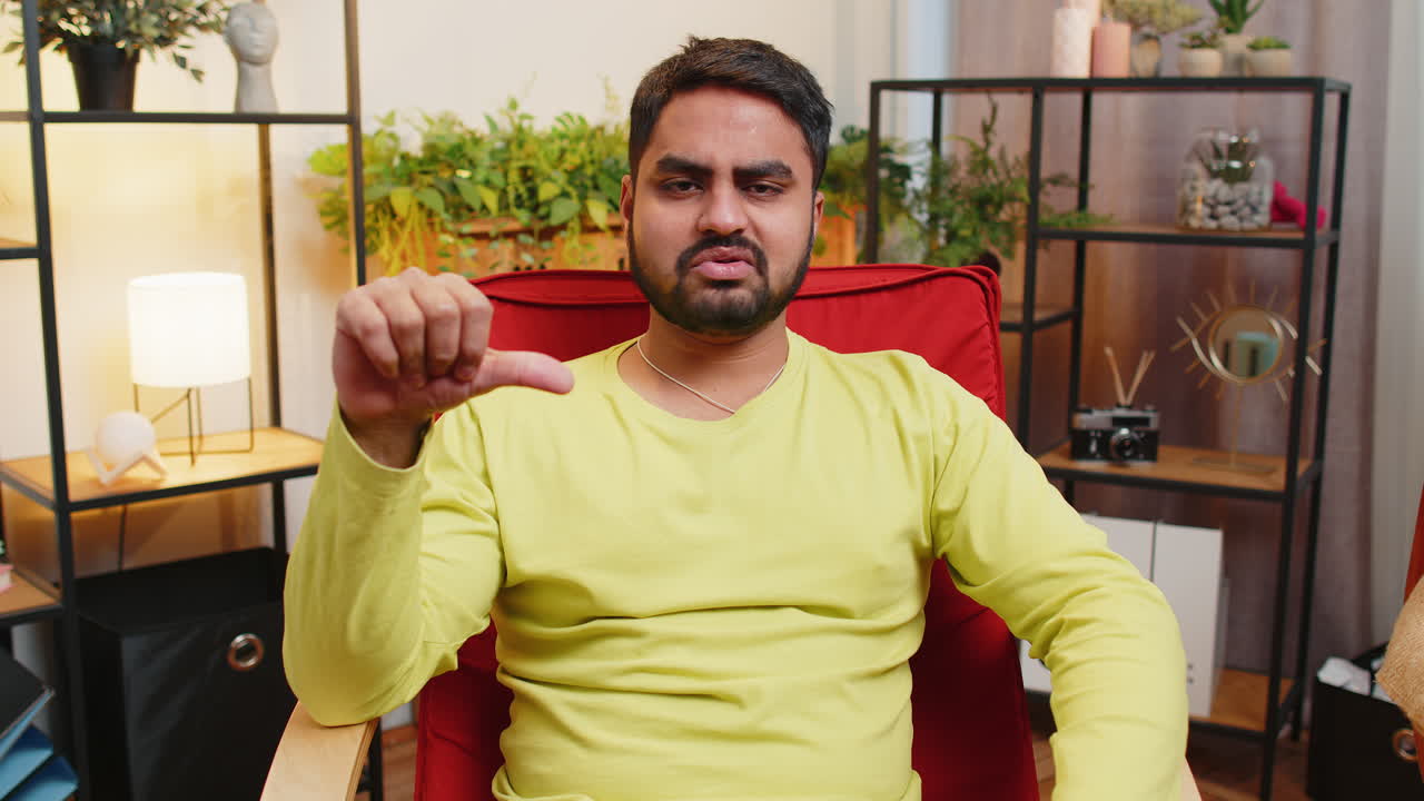 Upset arabian man showing thumbs down dislike bad work disapproval dissatisfied feedback at home