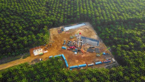 cinematic 4k drone footage of onshore drilling rig equipment structure for oil exploration and exploitation in the middle of jungle surrounded by palm oil trees during sunset and high oil price