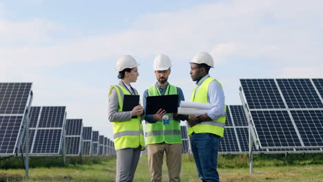 three multiethnics farm solar engineers talking while looking at blueprint on solar plantation