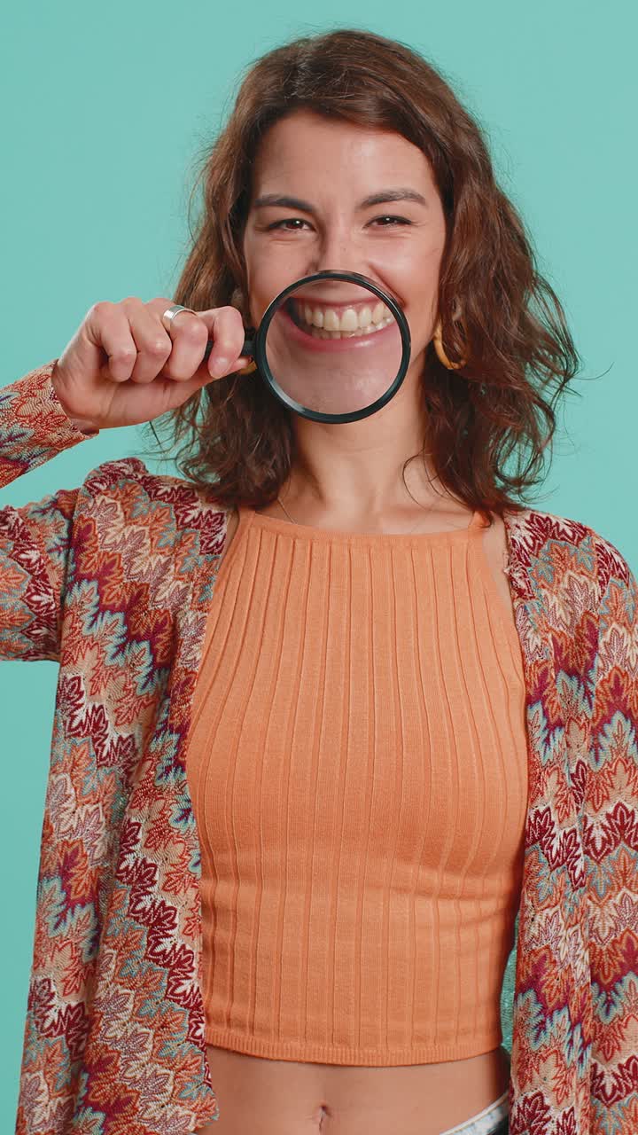 Donna con una lente di ingrandimento sui denti che guarda la telecamera mostrando una faccia sorridente e una bocca divertente