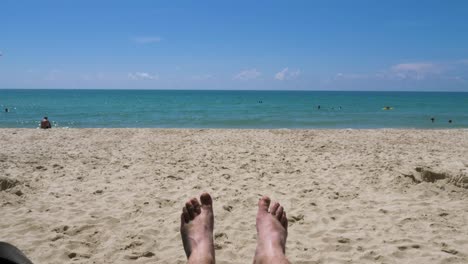 First-person-perspective-of-being-barefoot-and-lying-down-on-a-sunny-sandy-beach