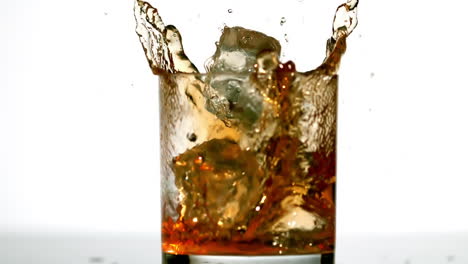 un cubo de hielo cayendo en un vaso de whisky