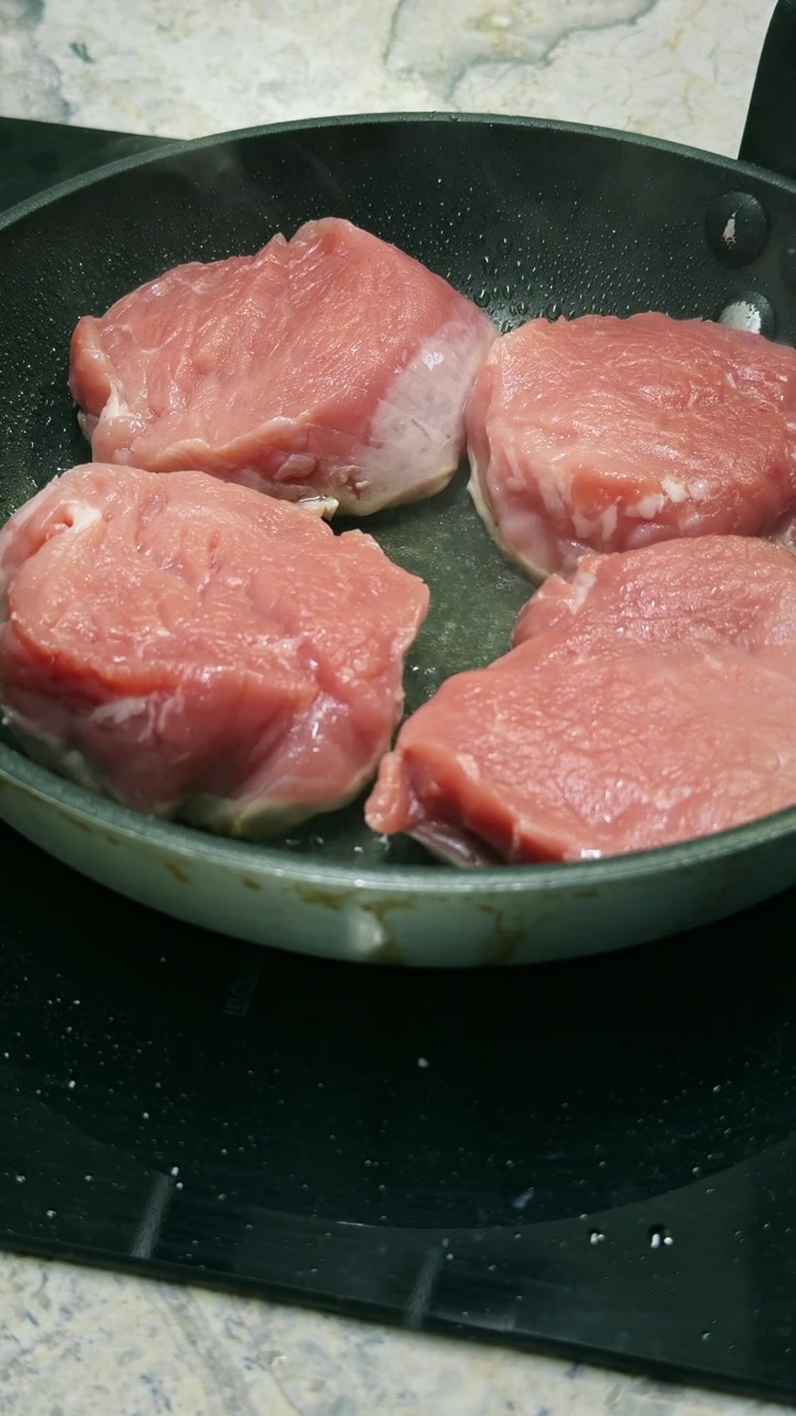 Close-up medali daging babi tenderloin mendesis di wajan saat membentuk kerak keemasan yang terpanggang. Rekaman persiapan makanan 4K vertikal