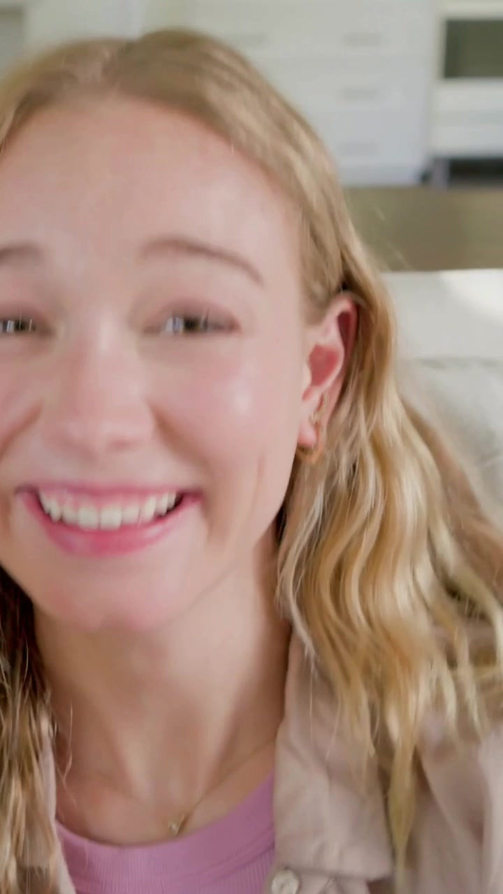 Vertical video: Laughing woman wearing tan shirt reacting to partner speaking on couch near kitchen