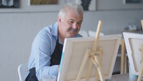 a female teacher shows a retired man how to draw a picture with paints and a brush at courses for the elderly. a senior man draws a picture to a group of pensioners