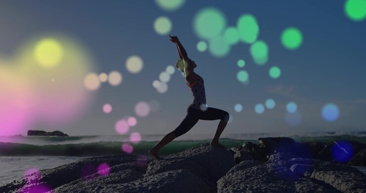 Donna che pratica yoga su una spiaggia rocciosa al tramonto