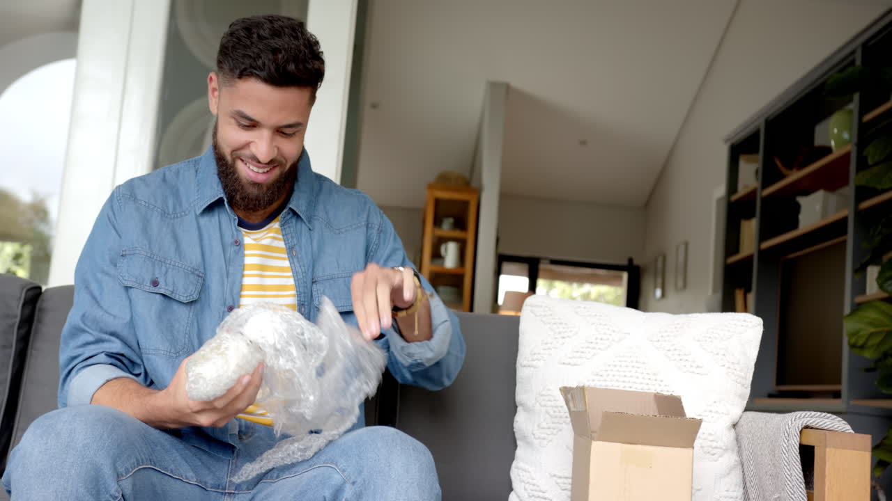 Unboxing package, man sitting on couch and smiling while opening bubble wrap