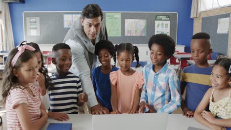 happy diverse male teacher and children using laptop in elementary school class, slow motion