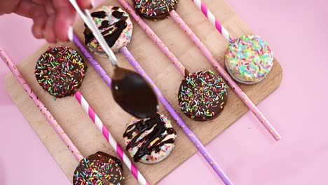 sweet delicious cake pops on wooden board and decorating with melted dark chocolate