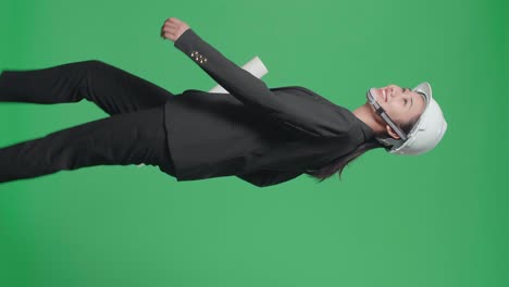 side view of smiling asian female engineer with blueprint looking around and shaking her head while walking in the green screen studio