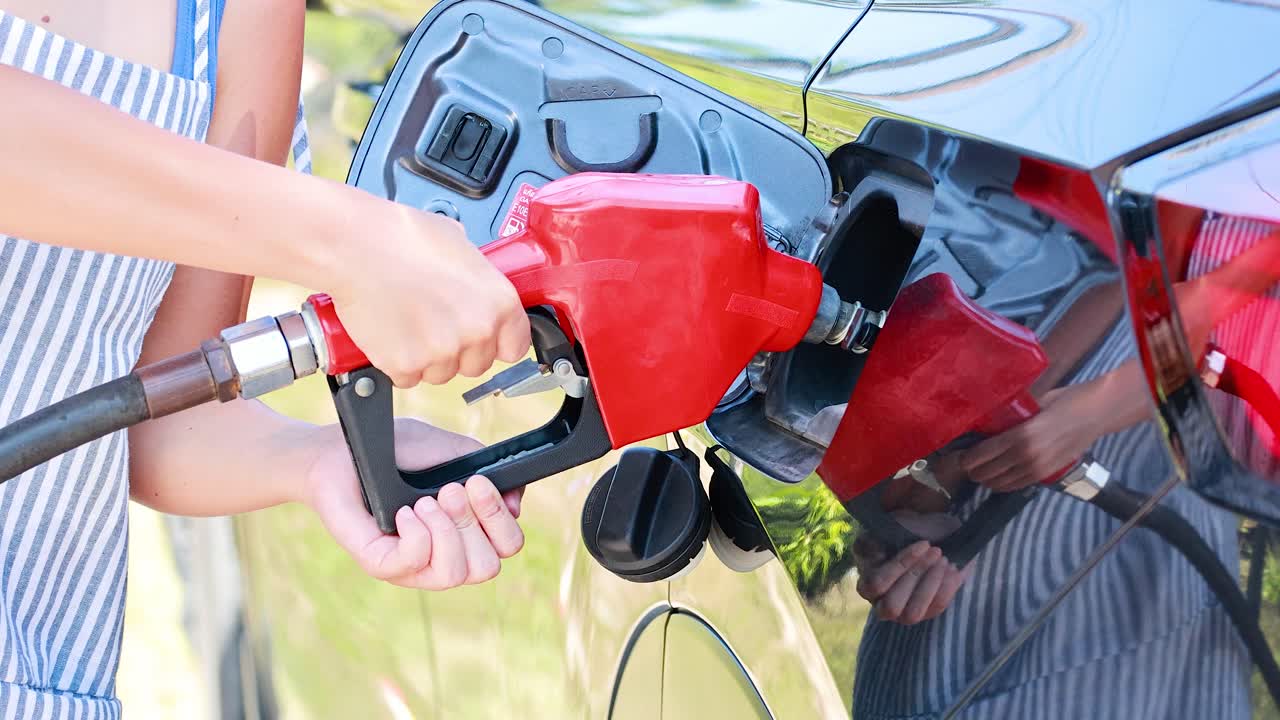 Person refuels vehicle with gasoline under bright daylight at outdoor gas station, close-up view