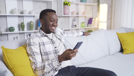 Happy-african-young-man-looking-at-his-phone-at-home,-texting.