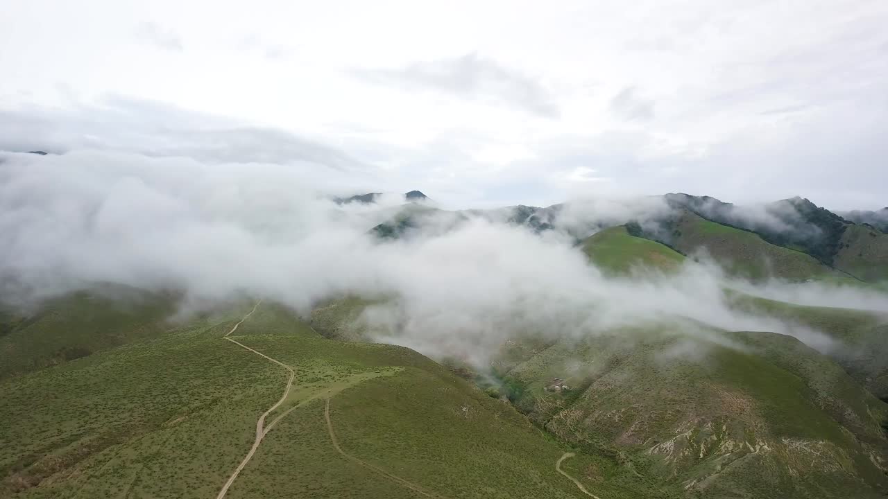 toma panorámica aérea a través de cadenas montañosas verdes abiertas a medida que la cubierta de nubes pasa por debajo del suelo