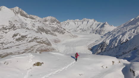 Toma-Aérea-En-Suiza-Con-Una-Persona-Caminando-Con-Raquetas-De-Nieve-En-Un-Día-Soleado-Con-Un-Glaciar-Detrás