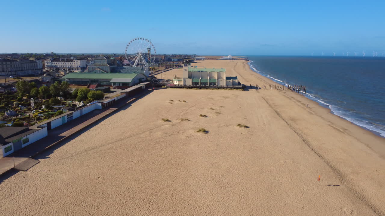 Great Yarmouth, English coast. Wellington Pier and beach aerial drone reverse shot. Iconic heritage British seaside town with amusement attraction and arcade piers popular in Victorian times