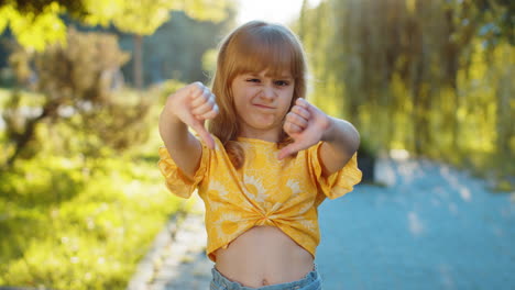 upset child girl showing thumbs down sign disapproval dissatisfied bad work mistake in city park