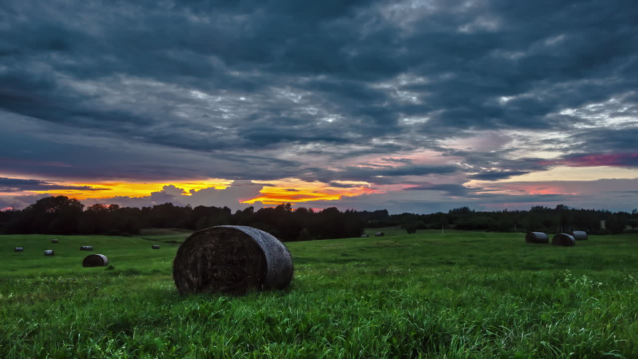 Moody clouds over green farm landscape time lapse with round hay bales