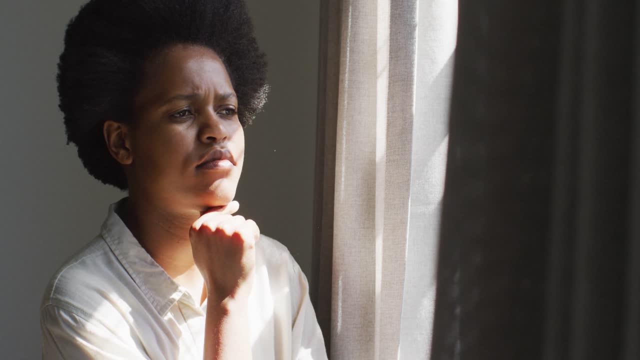Thoughtful african american woman looking through window in bedroom