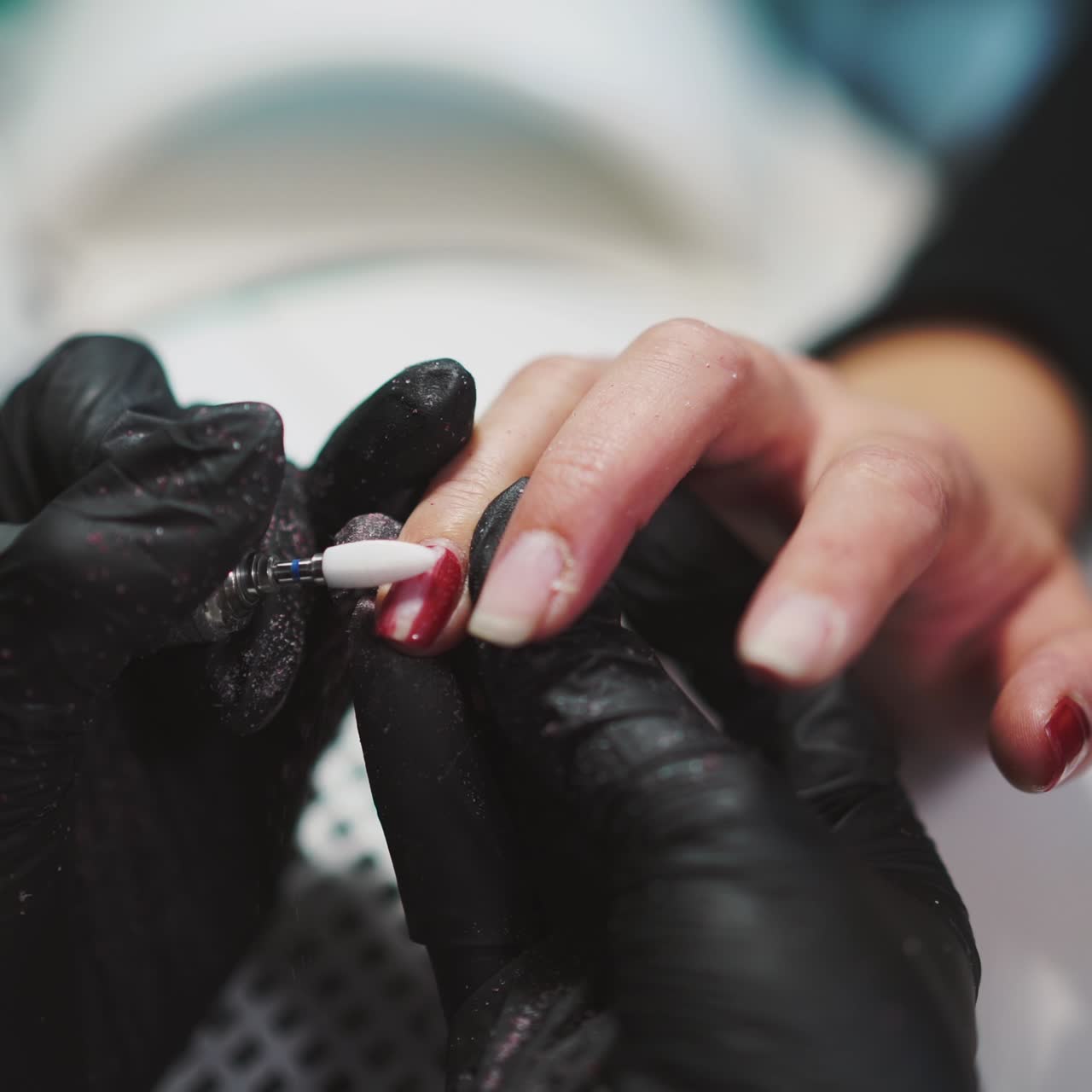 manicurist is removing red gel polish from the client's fingers with the using of professional equipment. Beauty salon
