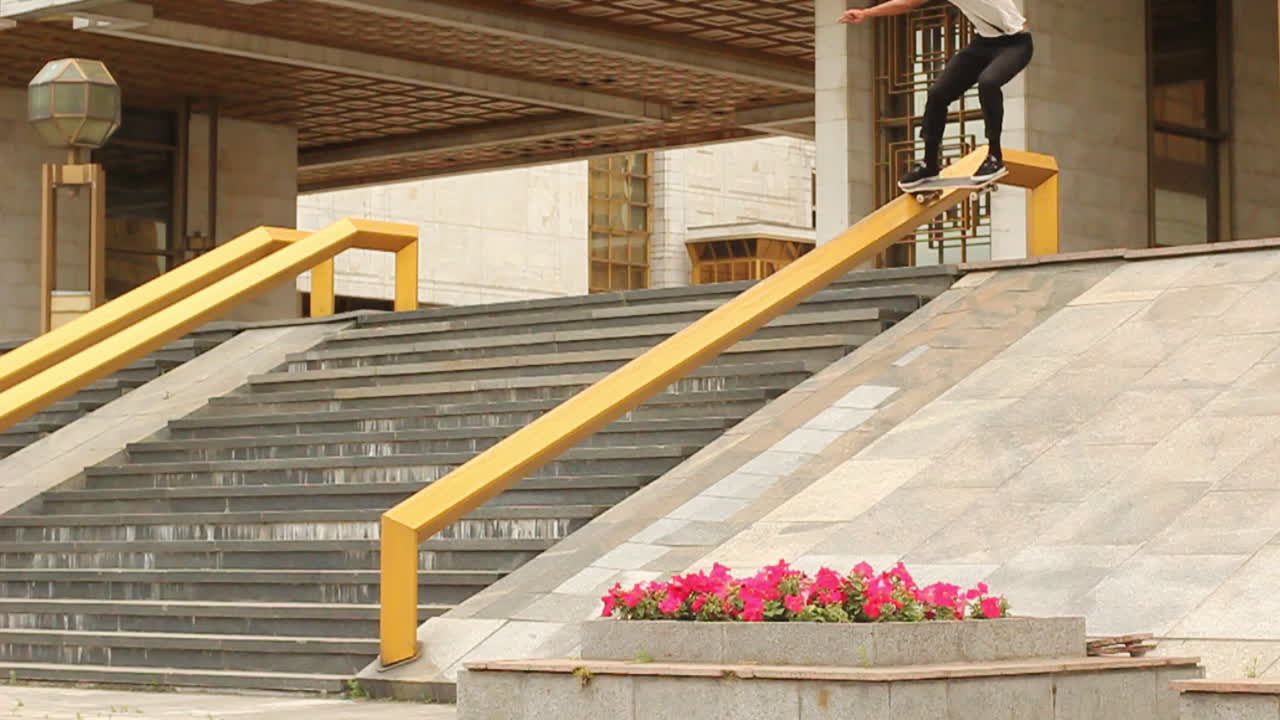 Dynamic shot of a skateboarder grinding down a yellow rail in front of monumental stairs and brutalist architecture