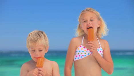 blond children eating water ices on the beach