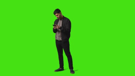joven enviando o leyendo un mensaje de texto en el teléfono móvil de pie contra la pantalla verde 1