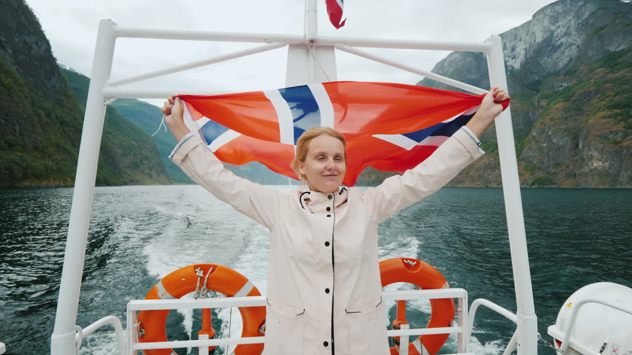 노르웨이 국기를 든 젊은 여성이 그림 같은 유람선 선미에 서 있다