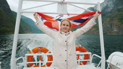 a young woman with the flag of norway stands at the stern of a pleasure boat a cruise on a picturesq