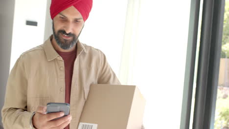 holding package, man in turban checking smartphone by window