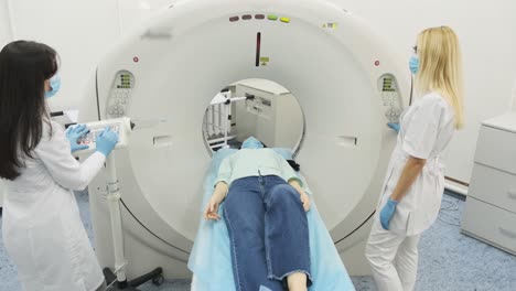 female patient is undergoing ct or mri scan under supervision of two qualified radiologists in mask and gloves in modern medical clinic. patient lying on a ct or mri scan table