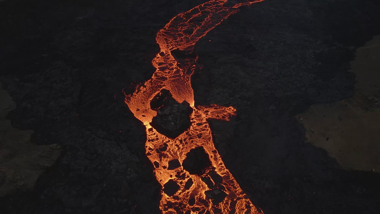 Aerial top-down forward over lava river flowing along black volcanic landscape