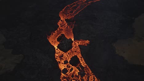 aerial top-down forward over lava river flowing along black volcanic landscape