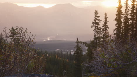 Misty-sunrise-over-tranquil-mountainous-landscape-with-glowing-sun,-trees-and-waterfall