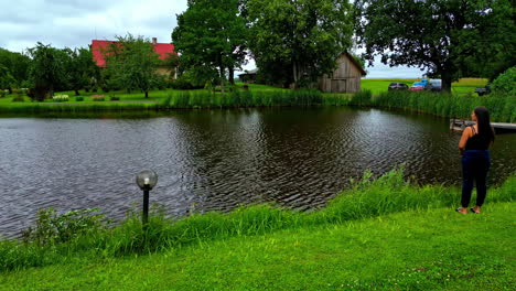 Beautiful-woman-fishing-near-rural-homestead-with-water-pond,-aerial-view