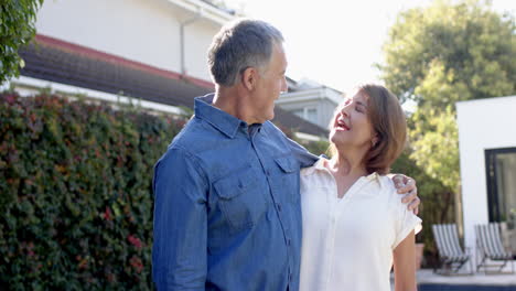 senior friends standing outside, smiling and looking at each other warmly