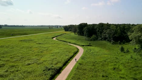 Aerial-view-of-person-riding-bike-on-bike-path-amongs-grassland-prarie,-battelle-darby-creek-metro-park,-Ohio