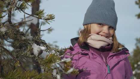 Portrait-of-Shy-girl-behind-pine-needle-branches-looking-at-camera-in-winter-forest