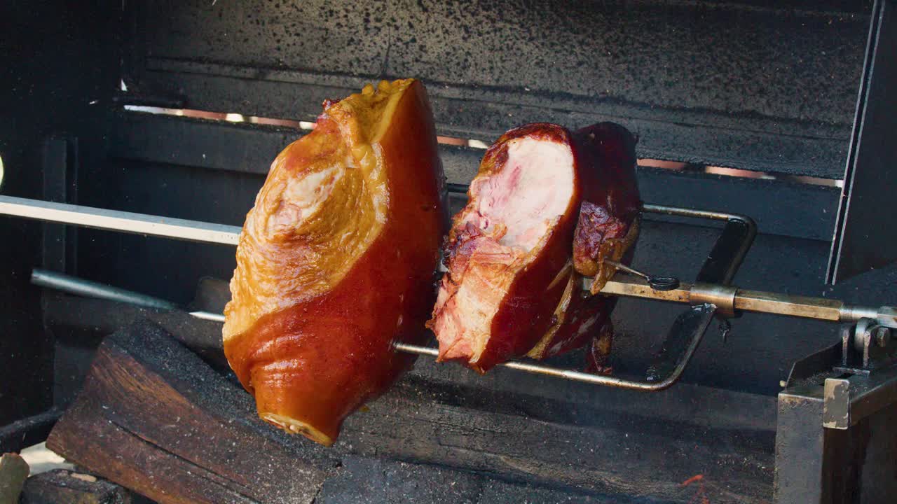 Juicy pork knuckle slowly rotates on spit above wood fire, traditional Czech street food preparation