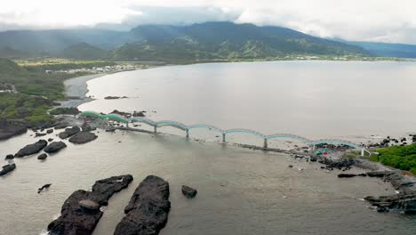 Vista-Aérea-Del-Famoso-Puente-De-8-Arcos-Que-Se-Extiende-Desde-El-Continente-Hasta-Un-Grupo-De-Pequeñas-Islas-En-Taiwán---Montañas-Dramáticas-Con-Nubes-En-El-Fondo