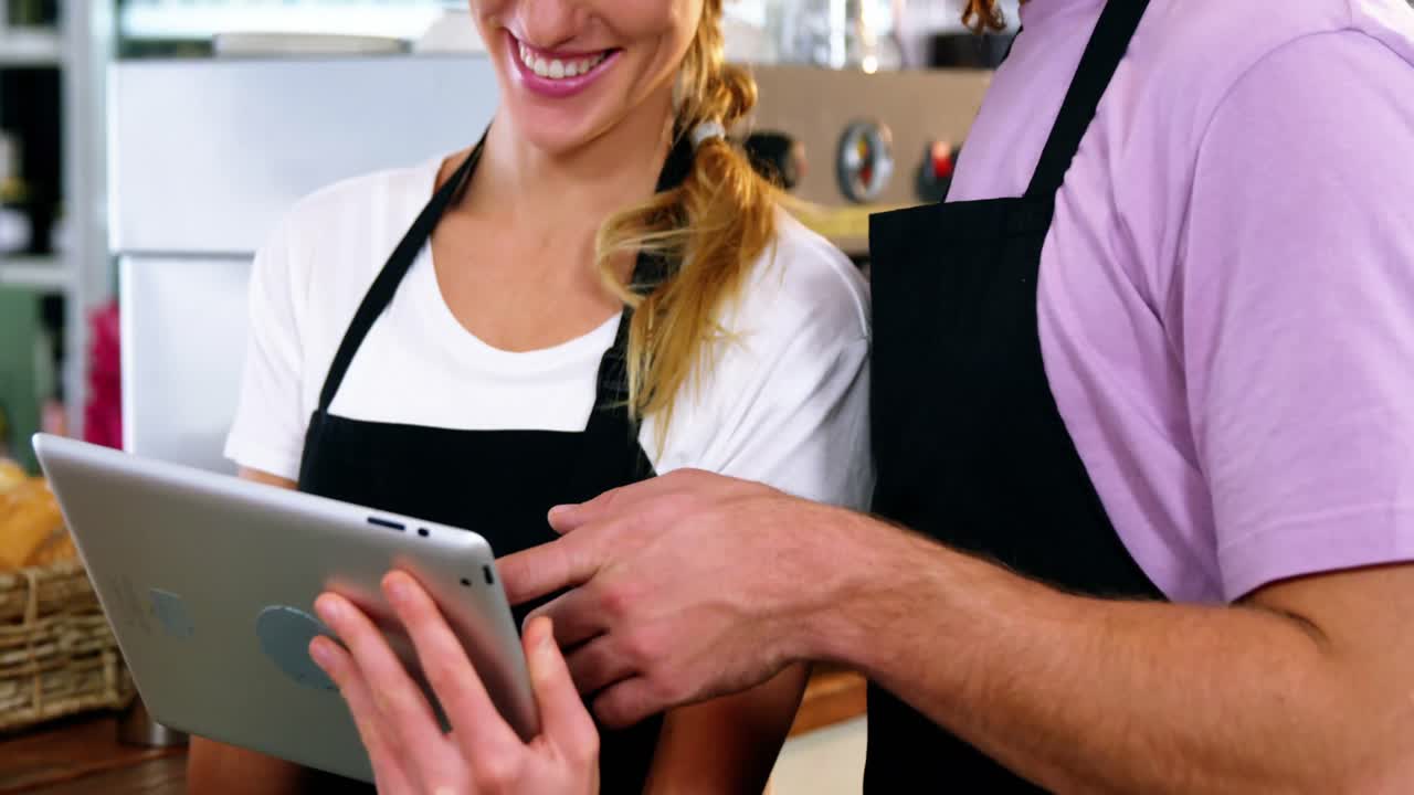 Smiling waiter and waitress using digital tablet at counter