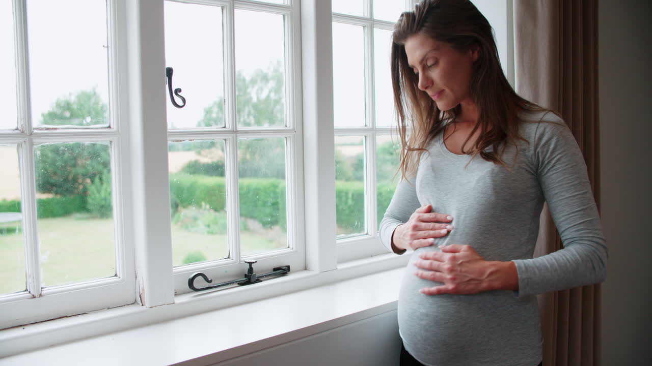 웃는 임신한 여성이 창문 에 서서 배를 들고