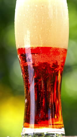 White foam becoming into dark beer with bubbles in glass. Foamy alcohol beverage in a tall glass on blur background. Close-up. Vertical video