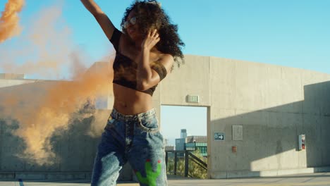 una mujer joven bailando afuera con una granada de humo al atardecer en el garaje del techo
