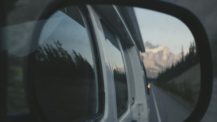 Reflection in the side mirror of an RV driving in in the rocky mountains of Canada, during sunrise hours, with huge mountains in the background