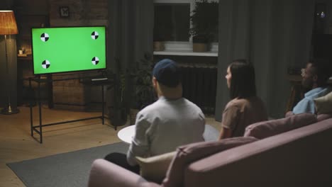 rear view of a three friends sitting on the couch looking at a screen and celebrating