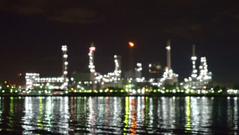 bokeh blurry background of petrochemical oil refinery and sea in industrial engineering concept, bangkok, thailand. oil and gas tanks pipelines in industry. modern metal factory with lights at night.